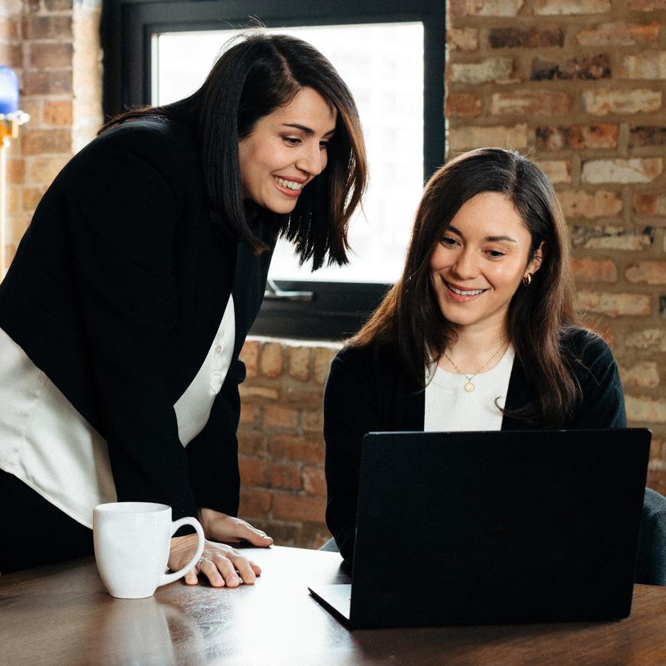 Two coworkers looking at a laptop with a coffee cup next to the laptop.